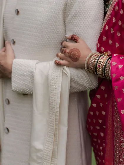 A close-up detail shot of the bride's hand with henna, resting on the groom's arm, symbolizing their union.