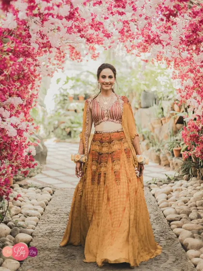 The bride, Bhavita, walking through a stunning floral archway, looking like she's stepped out of a fairytale.