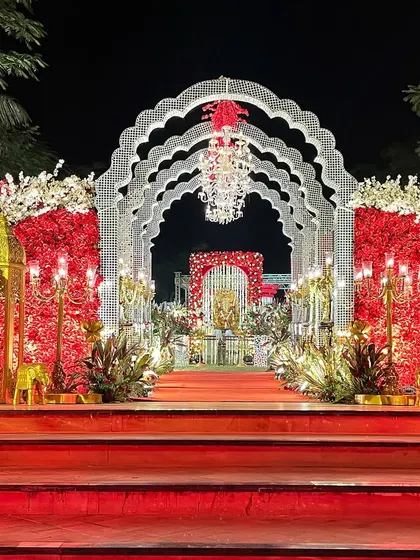 The entrance to your forever should be grand. This wedding walkway features layered white arches, crystal chandeliers, and rich red floral arrangements, setting a tone of pure opulence from the very first step.