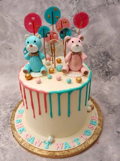 We create a sweet surprise with this teddy bear gender reveal drip cake. A pink and a blue teddy bear sit among colorful lollipops, while pink and blue drips run down the sides, making the reveal a truly delightful moment.