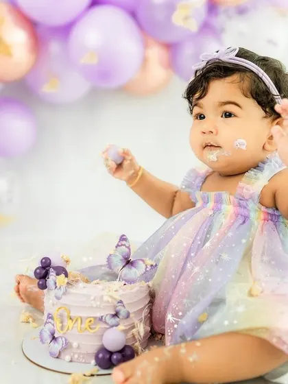 The aftermath of a delightful cake smash, with frosting on her fingers and a happy, curious expression.