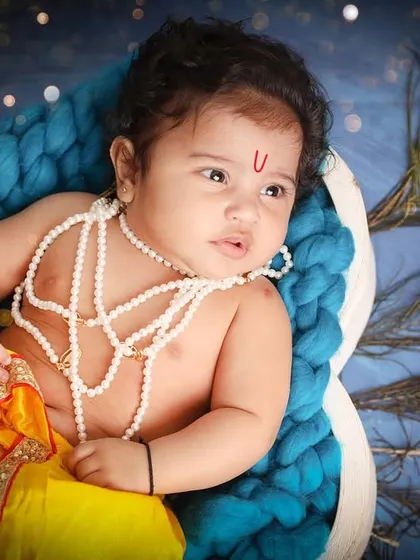 A thoughtful little Krishna, adorned with pearls and resting against a backdrop of peacock feathers. Every detail is carefully chosen to create an authentic and beautiful image.