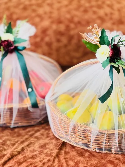 Two fruit baskets, one with pomegranates and oranges, the other with mangoes, beautifully wrapped for a wedding. This is a traditional and healthy addition to any trousseau.