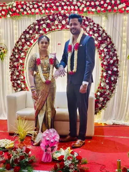 A full view of an engagement ceremony with a red rose arch, showing the couple and the traditional offerings arranged in front of the stage.