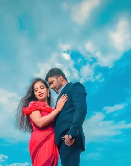A romantic close-up against the sky. The groom's dark suit creates a strong silhouette, allowing the bride and her red dress to be the main focus.