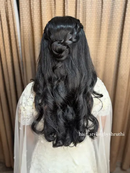 A half-up style featuring a braided crown and a small rose-shaped bun, with the rest of the hair in soft waves. This intricate detail adds a unique touch to a classic look.