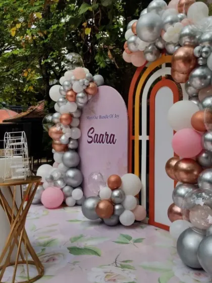 An angled view of the "Saara" naming ceremony decor. The organic balloon garland elegantly frames the custom-printed backdrop and the modern rainbow arch accent.