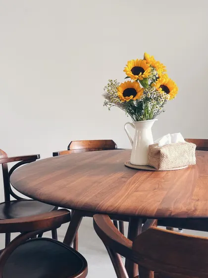 Our Volta Dining Table, crafted from rich walnut, finds its place in a customer's beautiful home. The round shape encourages conversation, while the warm wood tones, paired with sunflowers, create a welcoming and timeless dining experience.