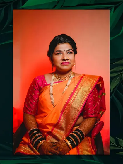 A stunning portrait of the bride in her orange and pink silk saree. The lighting highlights her features and the richness of her traditional Maharashtrian bridal look.
