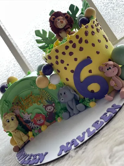 A side view of the jungle-themed cake, showing the leopard print texture and the playful monkey and elephant figures.