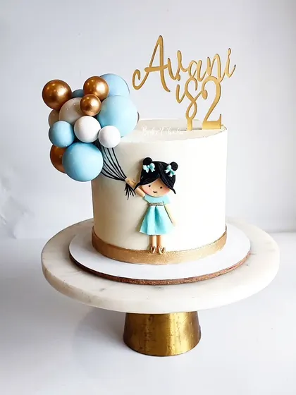 A full view of the simple yet elegant girl-with-balloons cake. The clean white ganache provides the perfect backdrop for the colorful, edible art.