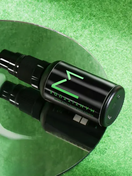 A creative shot for a men's face serum, showing the product on a mirror with a smear of lotion. The green textured background and reflection create a modern and edgy look.