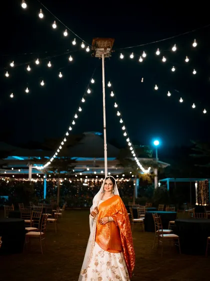 A stunning wide shot of the bride at her outdoor reception, standing under a canopy of stars and string lights.