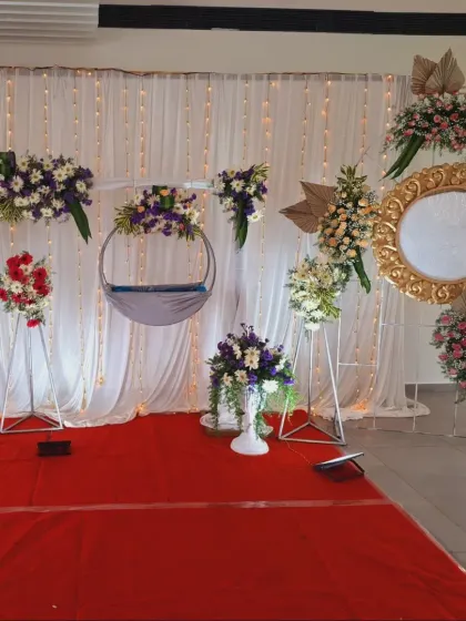 An elegant and modern naming ceremony setup with a hanging cradle, white drapes, and arrangements of white and purple flowers.