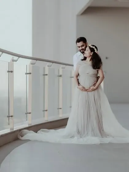 An elegant portrait of an expecting couple on a balcony. The mother-to-be is wearing a beautiful off-shoulder gown, creating a romantic and timeless maternity photograph.