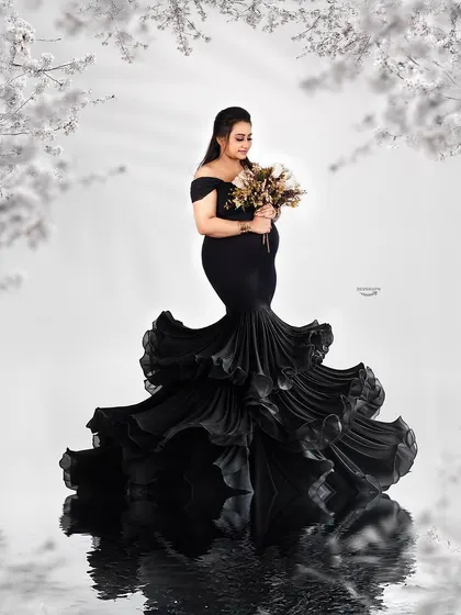 A stunning black and white composition featuring a dramatic ruffled mermaid gown. The floral frame and water reflection add layers of artistry to this elegant and timeless maternity portrait.