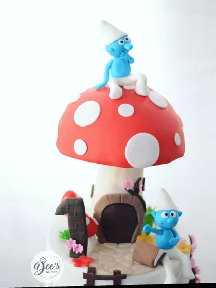 The centerpiece of the cake is this big, red mushroom house, complete with a Smurf lounging on top.