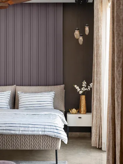 In this bedroom, I used a fluted panel headboard in a deep mauve color to create a textured accent wall. The design is complemented by beige furnishings and seashell pendant lights, resulting in a subtle yet elegant aesthetic.