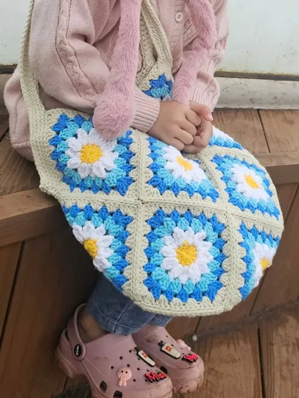 My Daisy Tote being modeled by my littlest helper. This shows the scale of the bag and how the bright, cheerful daisy granny squares look when worn.