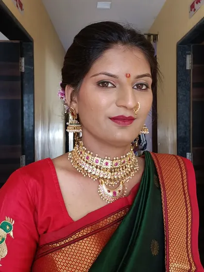 A classic look for a Maharashtrian bride in a green saree with a red border. The makeup features a bold red lip and defined eyes, paired with a traditional choker necklace.
