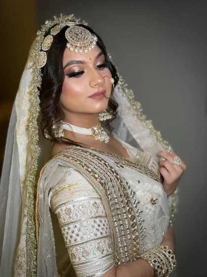 A classic bridal portrait in a white and gold saree. The makeup is soft and elegant, with a focus on clean skin and defined eyes.