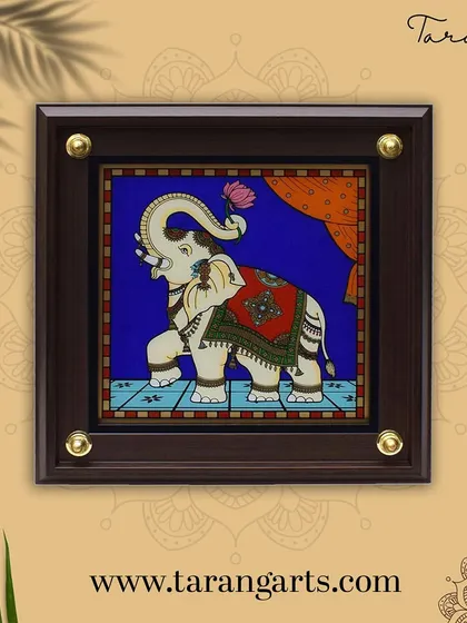 This glass painting of a decorated elephant holding a lotus is a symbol of purity and majesty. The artwork's vibrant colors and traditional motifs make it a beautiful and auspicious piece for any home.