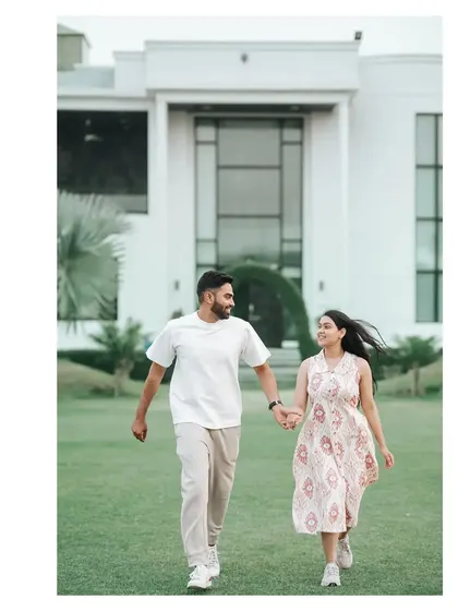A joyful shot of the couple running hand-in-hand on a beautiful lawn in front of a modern house.