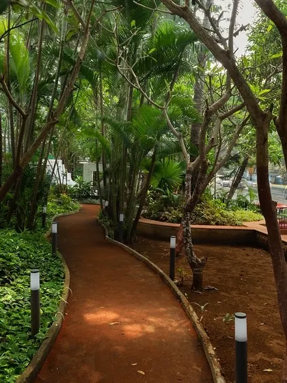 **Nepean Greens, Mumbai:** A winding pathway meanders through the trees, providing a peaceful walking route within the plaza. The careful placement of lighting ensures the space is safe and inviting even after sunset.