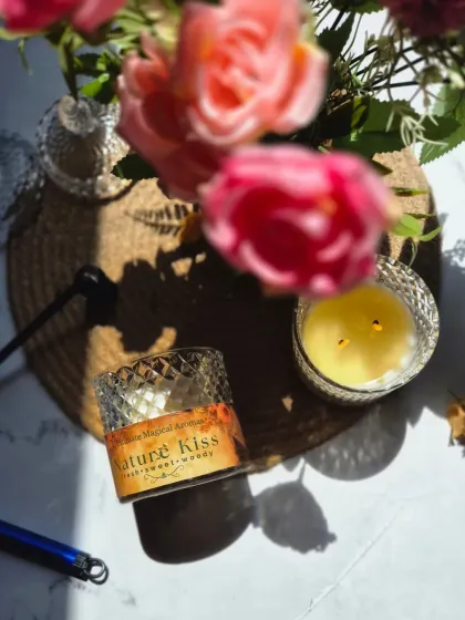 An artistic shot of the 'Nature Kiss' candle, capturing the sunlight and fresh flowers to evoke the fragrance's natural essence.