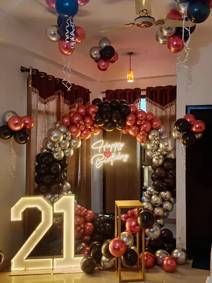 A chic 21st birthday party with a circular balloon arch in black, silver, and chrome red. The setup includes large light-up '21' numbers and balloons floating on the ceiling.