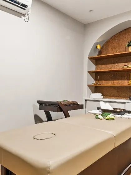 Every treatment room is a private retreat. Here, a comfortable massage bed is set against a feature wall with built-in shelving, allowing for a display of therapeutic oils and decor that enhances the holistic wellness experience.