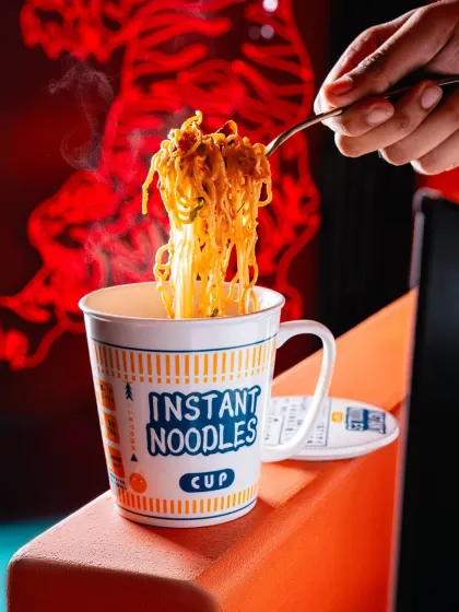 A steaming cup of instant noodles at Banng Bar. The dramatic backlighting and rising steam create a powerful visual that elevates a simple dish, making it look incredibly appealing.