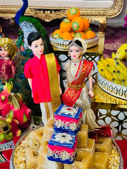 A close-up of a wedding couple doll arrangement. The dolls are dressed in rich red and white attire, placed on a platter of sweets, making it a perfect centerpiece.