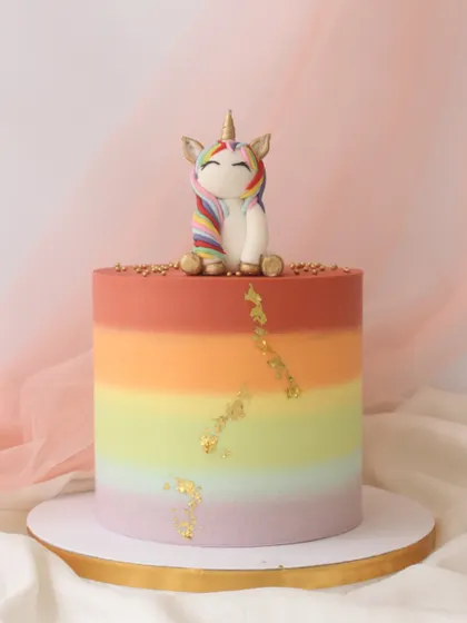 A beautiful unicorn cake with a smooth rainbow ombre buttercream finish. The cake is topped with a sweet unicorn figurine and accented with a touch of gold leaf.