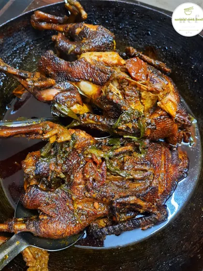 Two whole ducks being slow-cooked in a large pan. This method ensures the meat is incredibly tender.