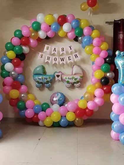 A baby shower for twins with a colorful balloon ring. The decor includes foil balloons of baby carriages and 'It's a Boy' and 'It's a Girl' feet.
