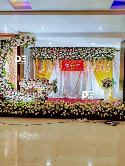 This naming ceremony stage features a crescent moon floral arrangement, adding a unique and modern touch to the traditional setup. The wide view shows the complete stage with floral pillars and backdrop.