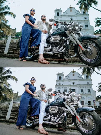A stylish portrait of the couple with a motorcycle, set against the iconic backdrop of a white Goan church and palm trees.