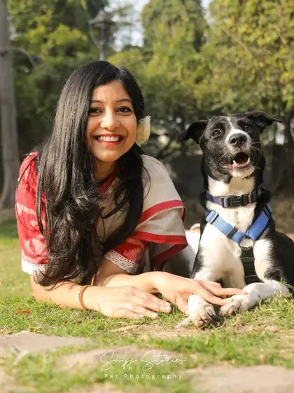 A smiling woman lies in the grass with her adopted black and white dog, Poppy, showcasing the happiness that adoption brings.