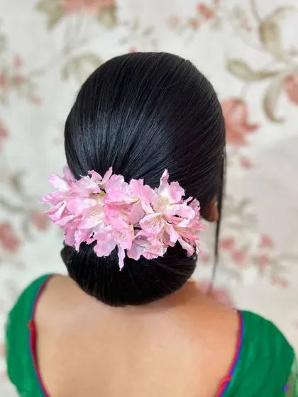 A classic, sleek donut bun adorned with a simple row of pink flowers, a very clean and elegant look.
