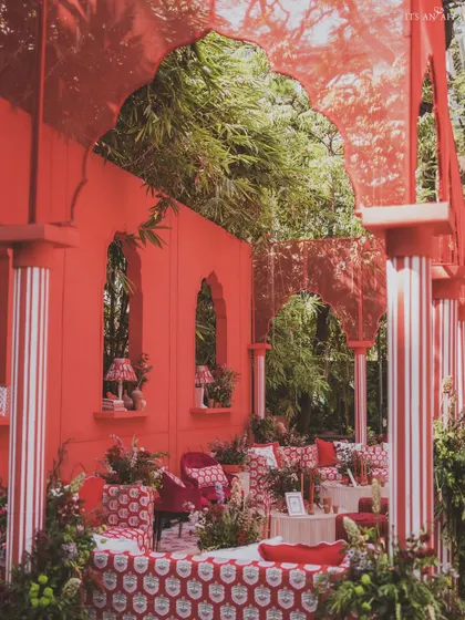 A view through the red arches, showcasing the layered design with custom-printed textiles and striped pillars.