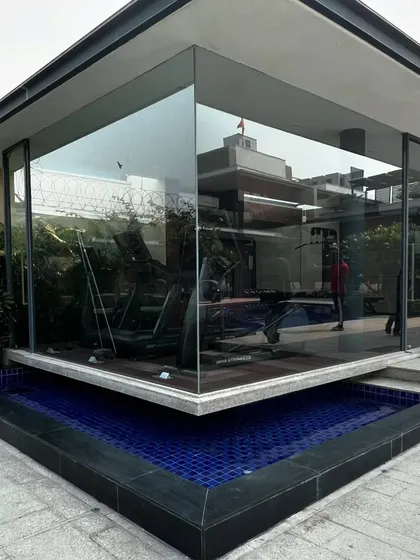 The glass-walled gym structure sits beside the pool, with its reflection creating a sense of expanded space.