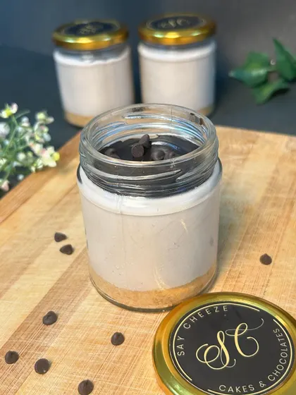 A chocolate chip cheesecake jar, with chocolate chips mixed into the creamy filling for a delightful texture. The branded lid makes it a perfect gift.