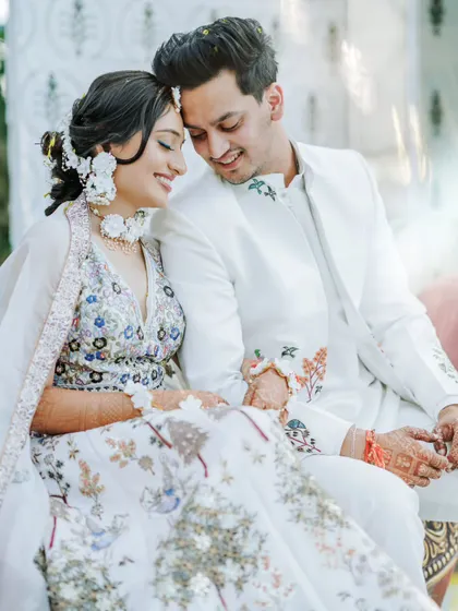 An intimate portrait of the couple in matching white outfits, sharing a quiet, happy moment together. The intricate floral embroidery on their clothes adds a beautiful detail.