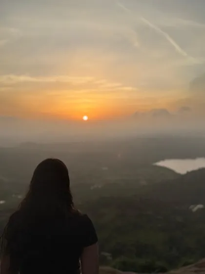 Another beautiful shot of a trekker watching the sunrise at Uttari Betta, with a lake visible in the distance.