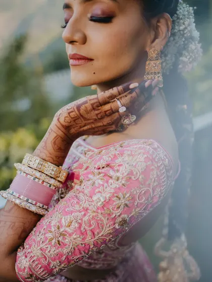 A detailed close-up of the bride's intricate henna, jewelry, and the beautiful embroidery on her pink lehenga. We believe in capturing the small details that complete the bridal story.