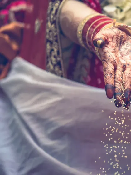 An artistic shot of a bride's hands performing a ritual. The falling grains and detailed henna create a visually compelling image rich with symbolism.
