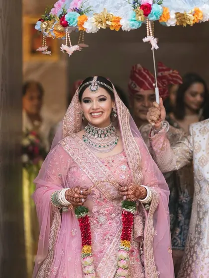 A happy bride making her entrance. Her makeup is soft and pretty, with a pinkish glow that perfectly matches her pastel pink lehenga.