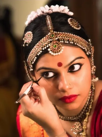 A behind-the-scenes shot of a Bharatanatyam dancer applying eye makeup before a show. The preparation is as meticulous as the performance itself.