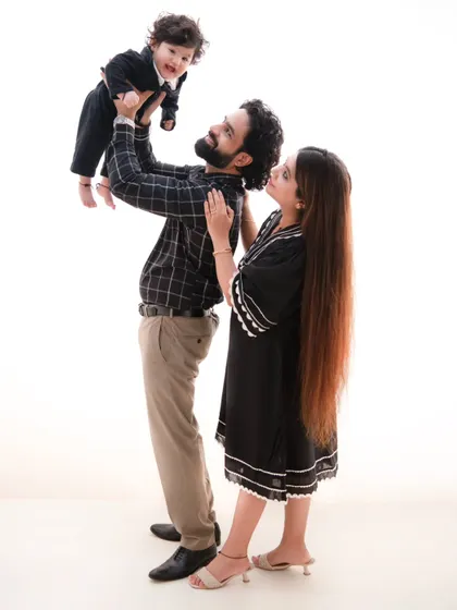 A moment of adoration. The father lifts his son, and the mother looks on with a smile, creating a dynamic and loving family portrait.